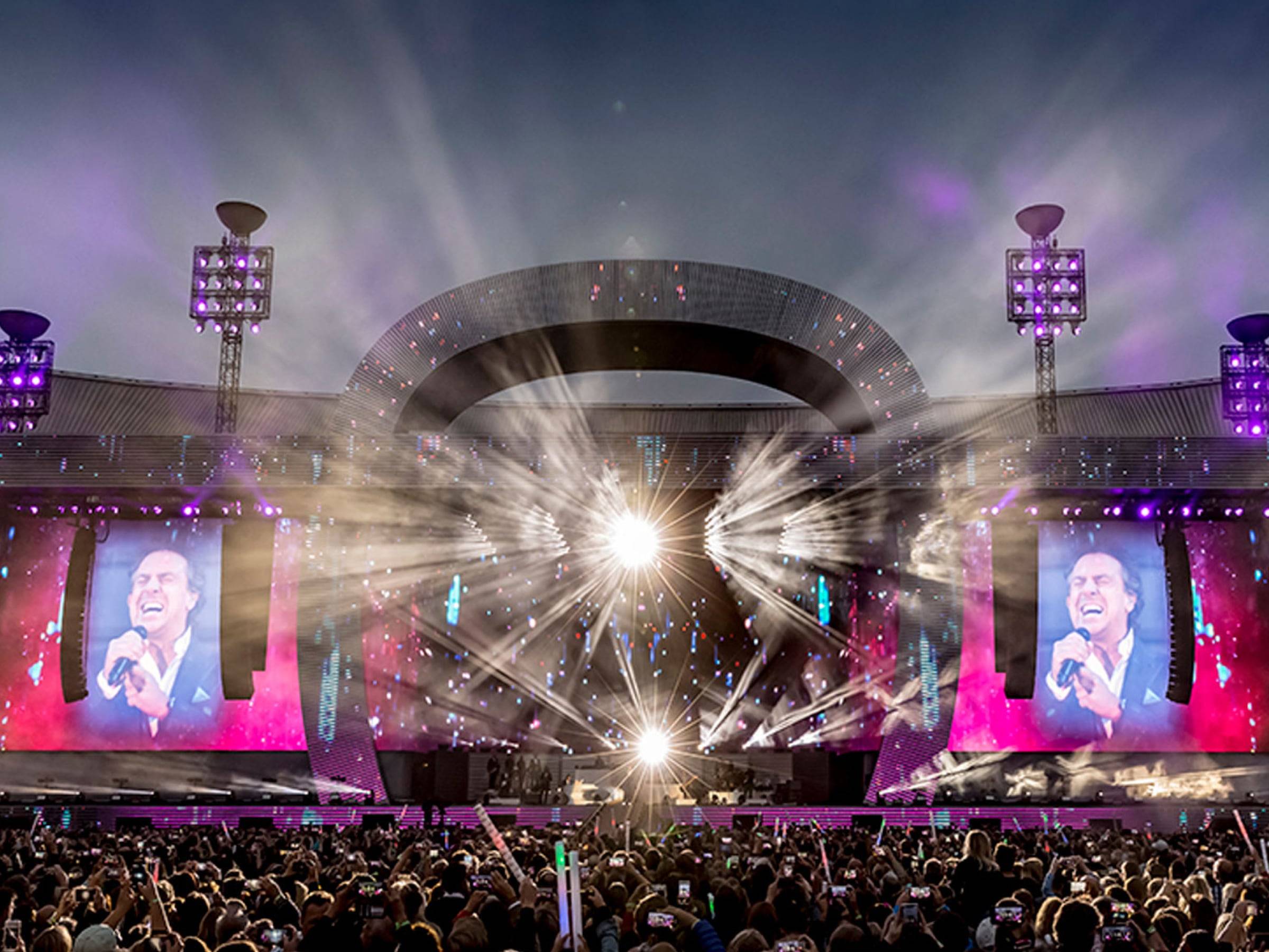 A concert venue showing lights and big digital display screens displaying the video of the performer to the audiences.