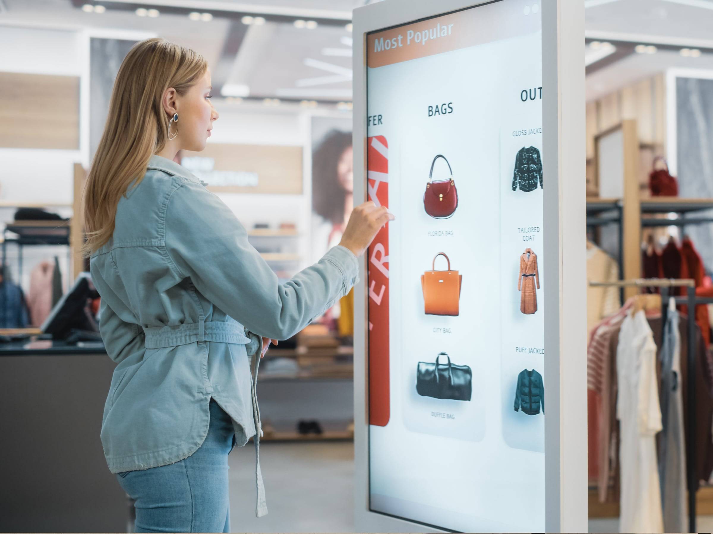a woman looking at bags on an interactive digital kiosk.